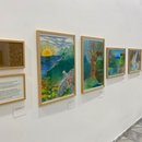 Eine Reihe gerahmter, farbenreicher Landschaftsbilder ist entlang einer wei&szlig;en Wand angeordnet. Die Werke zeigen unter anderem Meer, Sonne, Berge, B&auml;ume und fantasievolle Naturmotive.